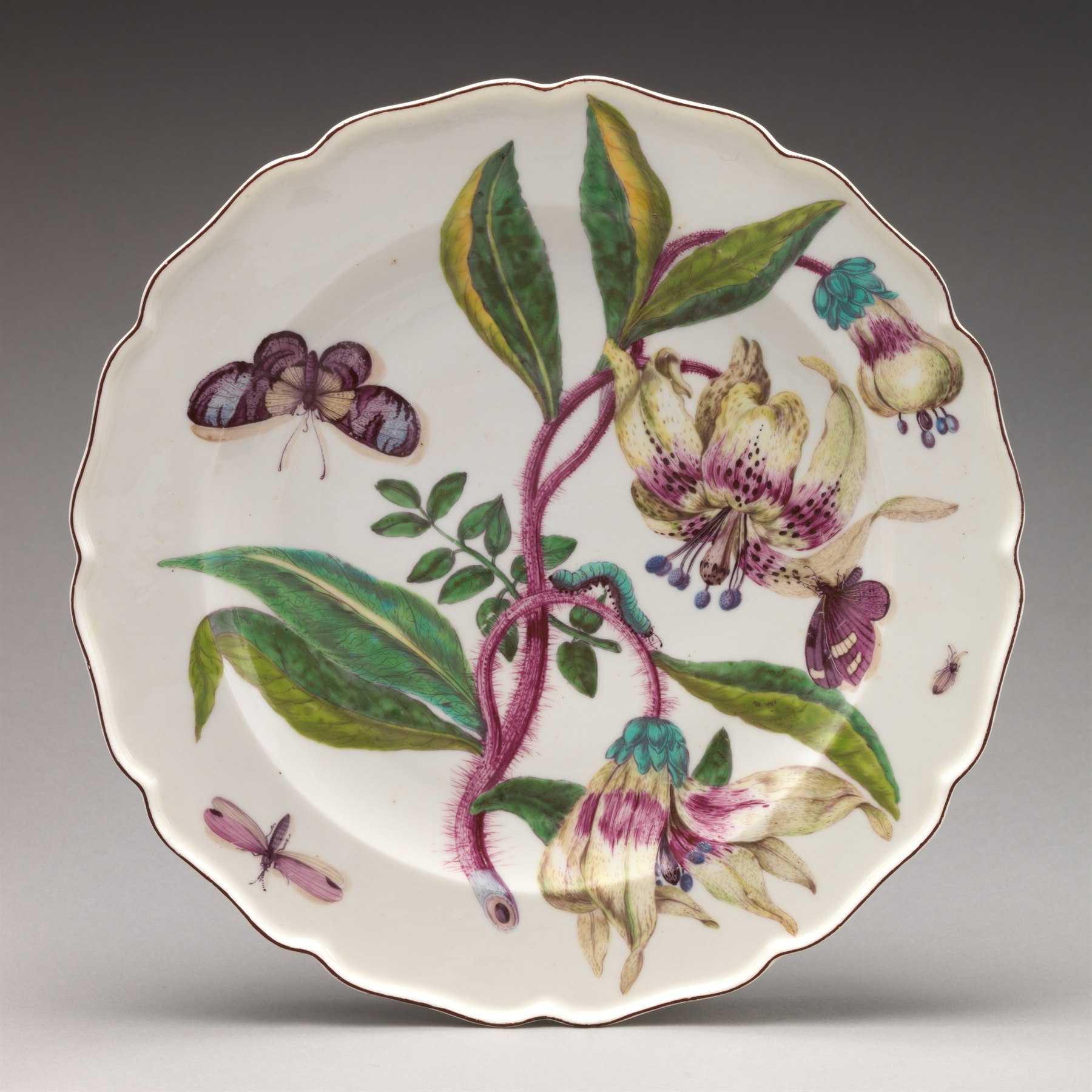 A scalloped porcelain plate is painted with lilies, leaves, butterflies, and insects.